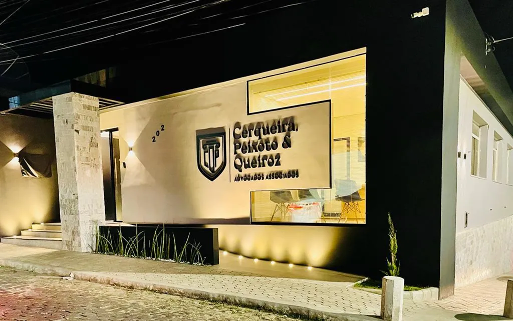 Fachada iluminada do escritório, com o logotipo na parede, à noite.
